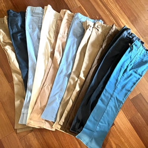 Peut inclure: Une collection de 12 paires de pantalons dans différentes nuances de bleu, marron et beige. Les pantalons sont disposés en éventail, les couleurs les plus foncées en bas et les couleurs les plus claires en haut.
