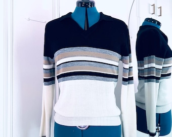 May include: A striped long-sleeved sweater with a black, white, and gray color scheme. The sweater has a v-neck and a ribbed collar.