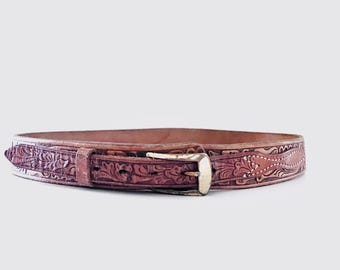 May include: A brown leather belt with detailed floral and geometric patterns. It has a gold-coloured buckle and a matching belt loop. The leather has a warm tone, and the design is textured and detailed.