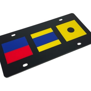 May include: Black license plate with three nautical flags. The first flag is red and blue, the second is yellow and blue, and the third is yellow with a black circle in the center.