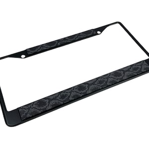 May include: Black metal license plate frame with a snakeskin pattern on the top and bottom edges.