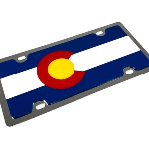 May include: A silver license plate frame with the Colorado state flag. The flag features a blue background with a white stripe, a red circle with a yellow center, and a white stripe.