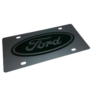 May include: Black metal license plate frame with a silver Ford logo in an oval shape.