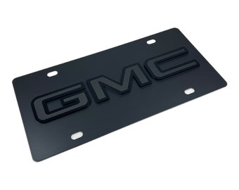 Może przedstawiać: Czarna metalowa ramka na tablicę rejestracyjną z wypukłym, szarym logo GMC.