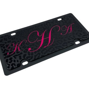 May include: Black license plate cover with a leopard print pattern and the letters "KHA" in pink.