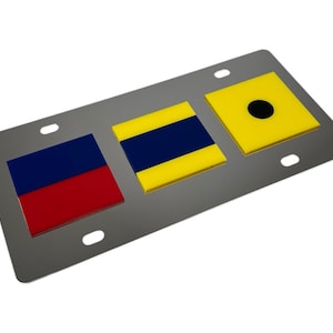 May include: Three metal license plate frames with nautical signal flags. The first frame has a red, white, and blue flag. The second frame has a yellow flag with a blue stripe. The third frame has a yellow flag with a black circle.