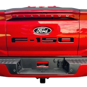 May include: Rear view of a red Ford F-150 pickup truck with black "F-150" and "PLATINUM" lettering on the tailgate.