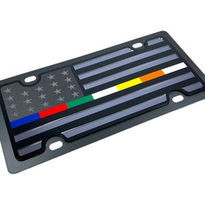May include: A black metal licence plate with a thin grey and black American flag design. The flag has a thin blue, red, green, yellow and orange stripe across the middle.