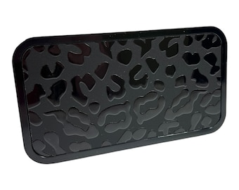 May include: A black rectangular belt buckle with a raised leopard print design.