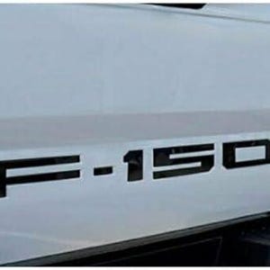 May include: Black F-150 emblem decal for a truck. The decal is made of vinyl and is designed to be applied to the tailgate of a truck.