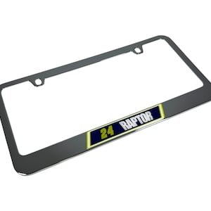 May include: A chrome license plate frame with the text "24 RAPTOR" on a navy blue and yellow background. The frame is rectangular with rounded corners and mounting holes.