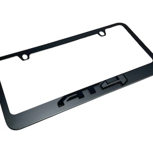 May include: Black license plate frame with the letters "4x4" in a bold, stylized font. The frame has a rectangular shape with rounded corners and mounting holes. The frame is made of a matte black material.
