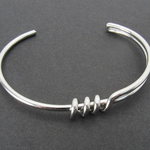 May include: A silver bangle bracelet with a twisted design. The bracelet is open and has a simple, minimalist style.