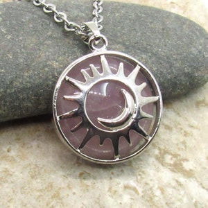 May include: A silver necklace with a round pendant featuring a pink sun and moon design.