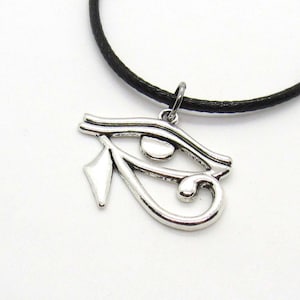 Puede incluir: Un collar con un colgante de plata con el ojo de Horus, en un cord&oacute;n negro. El colgante es una representaci&oacute;n detallada del s&iacute;mbolo egipcio antiguo.