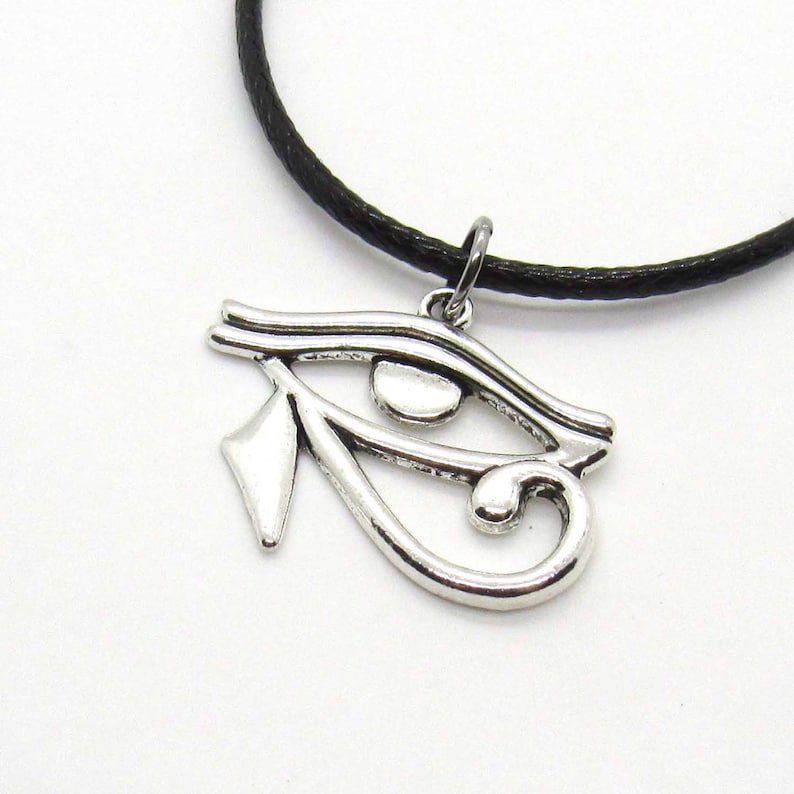 Puede incluir: Un collar con un colgante de plata con el ojo de Horus, en un cord&oacute;n negro. El colgante es una representaci&oacute;n detallada del s&iacute;mbolo egipcio antiguo.