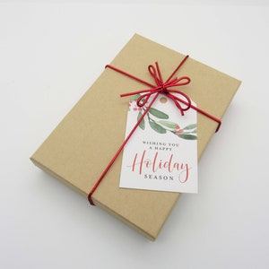 May include: A brown gift box tied with a red ribbon and a gift tag that says "Wishing you a happy Holiday Season". The tag has a watercolor design of green leaves and red berries.