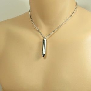 Puede incluir: Un collar de cadena de plata con un colgante de bala de plata.