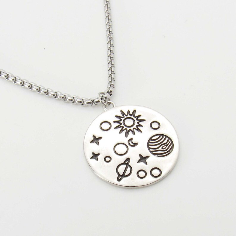 May include: A silver necklace with a round pendant featuring an engraved design of the sun, moon, stars, and planets.