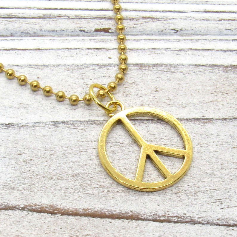 May include: A gold peace sign pendant necklace with a ball chain.