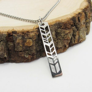 May include: A silver necklace with a pendant featuring a geometric design of overlapping leaves. The pendant is rectangular and has a cutout design.