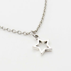 Pode incluir: Um colar de corrente de prata com um pingente em forma de estrela. A estrela tem um centro aberto.