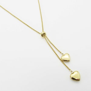 May include: A gold chain necklace with a sliding clasp and two heart-shaped charms.