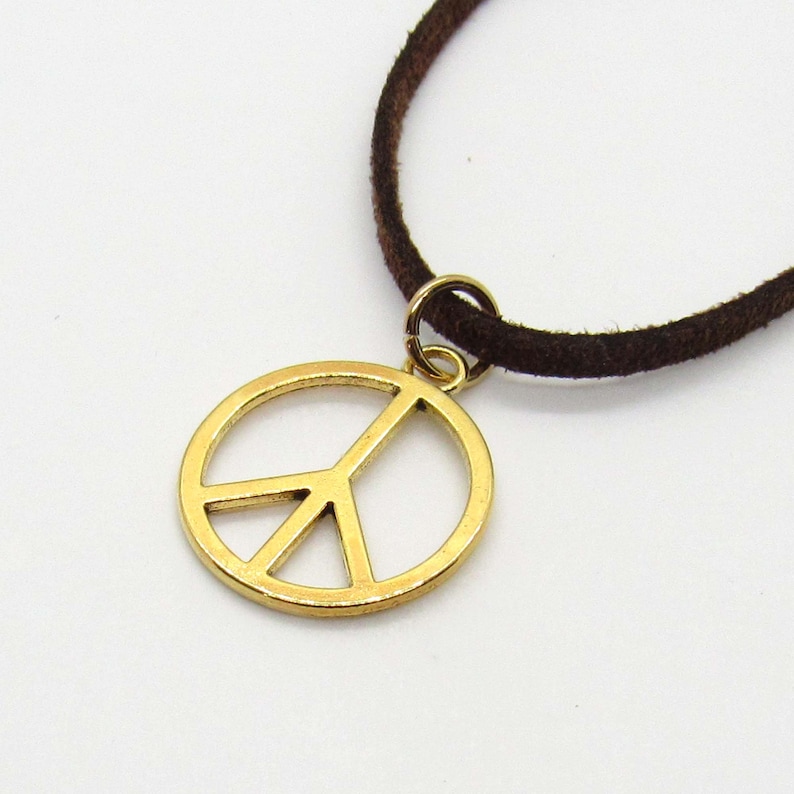 May include: A gold peace sign pendant necklace with a brown suede cord.