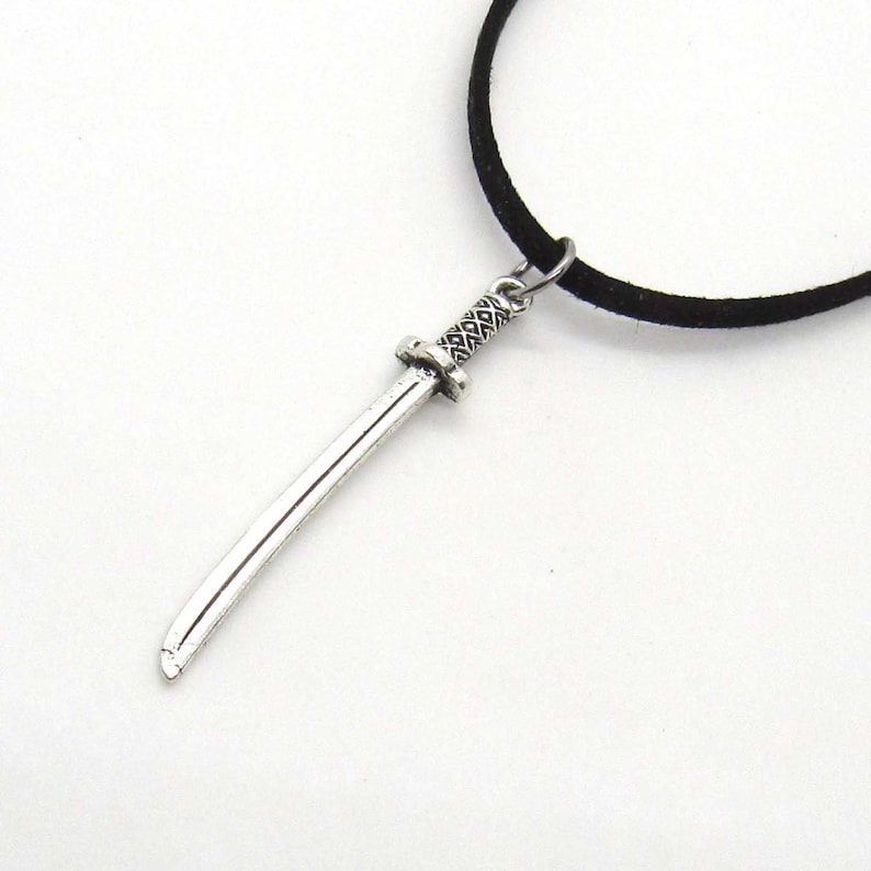 Puede incluir: Un collar de cord&oacute;n de gamuza negro con un colgante de espada de plata.