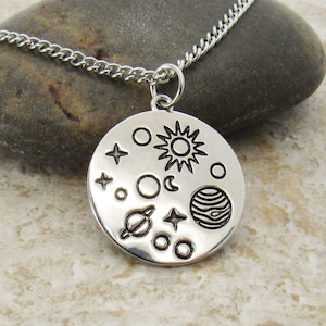 May include: A silver necklace with a round pendant featuring a stylized design of the sun, moon, stars, and planets.