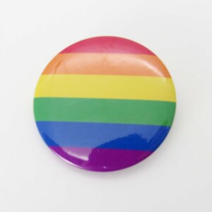 Op de afbeelding: Een ronde knop met de kleuren van de regenboog-pride-vlag: rood, oranje, geel, groen, blauw en paars.