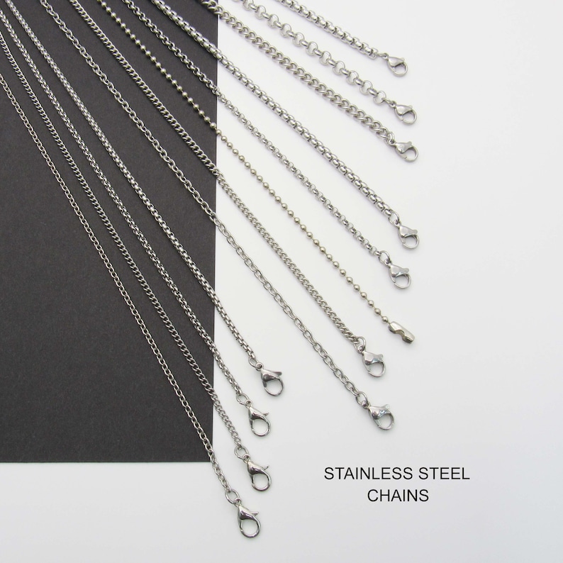 May include: A variety of silver stainless steel chains with lobster claw clasps. The chains are arranged in a fan shape on a white and black background. The text "STAINLESS STEEL CHAINS" is printed below the chains.
