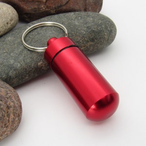 May include: A red metal keychain pill container with a silver ring.