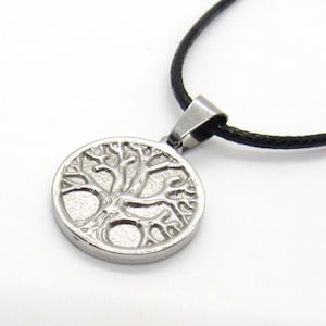 May include: A silver necklace with a round pendant featuring a tree of life design. The pendant is attached to a black cord.