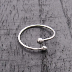 May include: A silver ring with two round, textured balls on the ends.