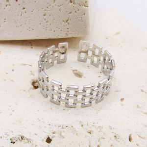 May include: A silver ring with a geometric design. The ring is made of a series of connected squares.