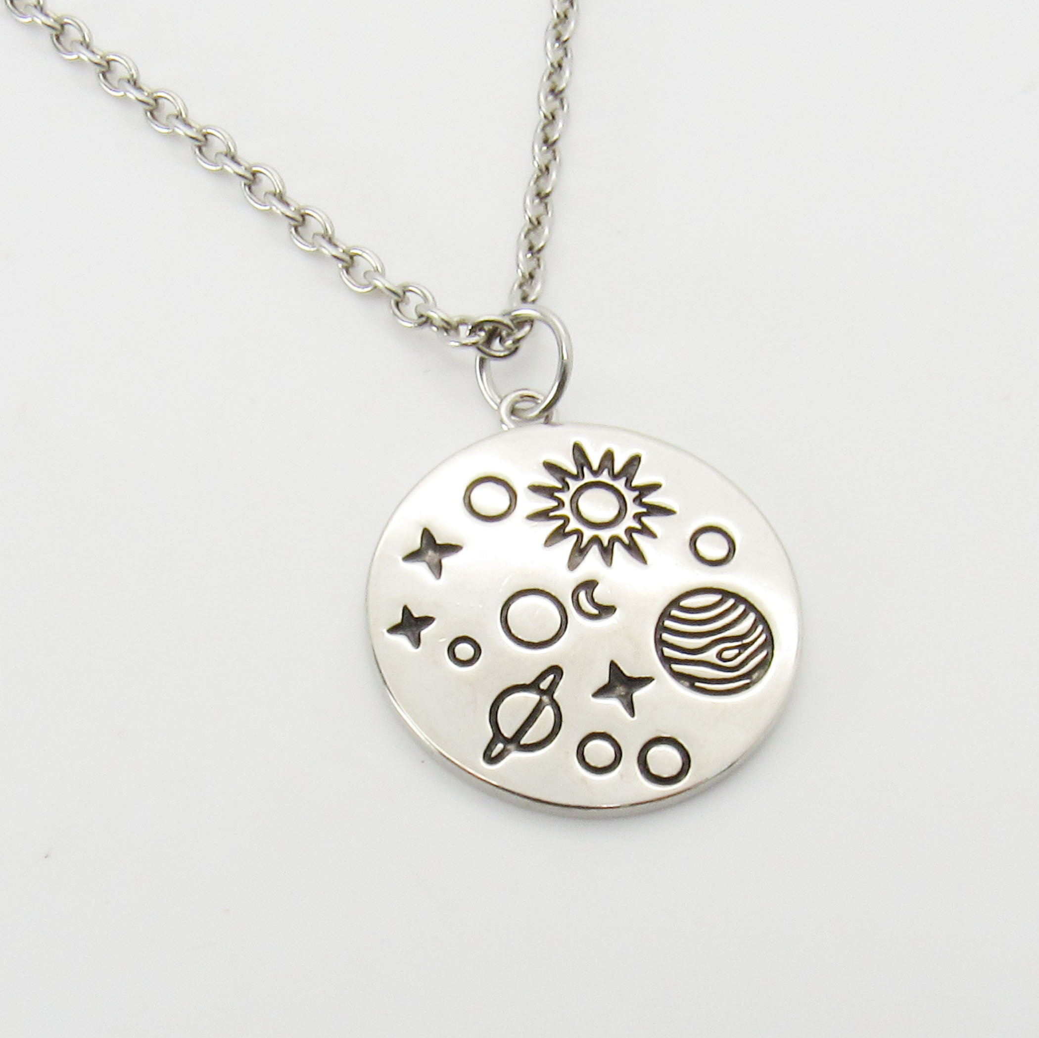 May include: A silver necklace with a round pendant featuring a sun, moon, stars, and planets. The pendant is engraved with a celestial design.