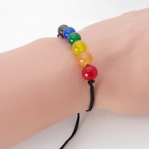 May include: A rainbow colored beaded bracelet with a black cord. The beads are round and made of semi-precious stones.