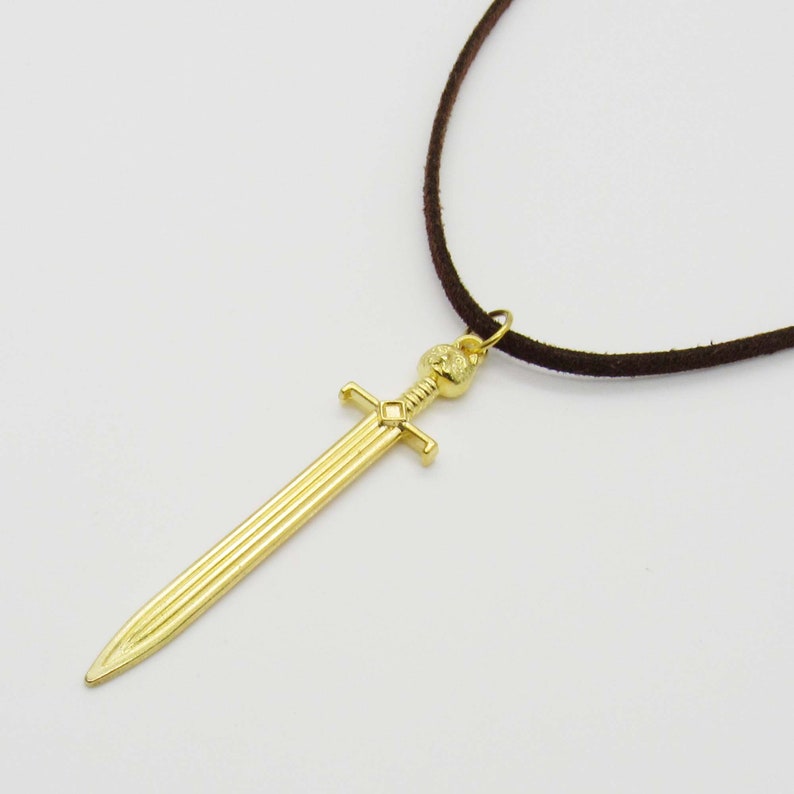 Pode incluir: Um colar com um pingente de espada dourada em um cord&atilde;o marrom.
