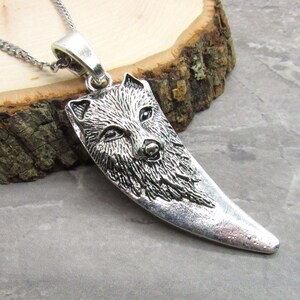 May include: Silver pendant necklace featuring a wolf's head design. The pendant is shaped like a wolf's fang and has a detailed, textured surface.