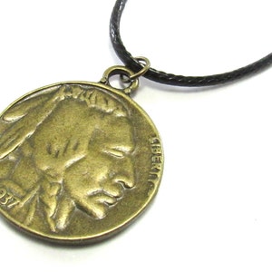 May include: A bronze-coloured pendant necklace featuring a 1937 Buffalo nickel coin with the profile of an American Indian on one side and the word "LIBERTY" on the other. The necklace has a black cord.