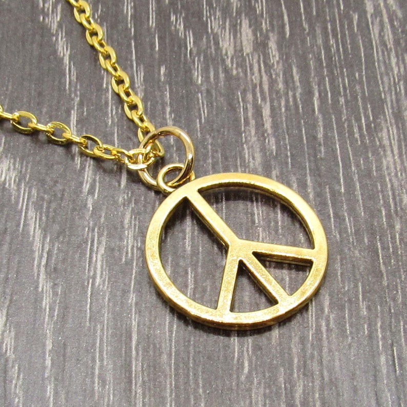 May include: A gold chain necklace with a peace sign pendant. The pendant is a simple, circular design with a peace symbol inside.