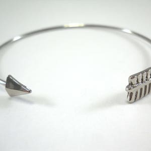 May include: A silver bangle bracelet with a pointed arrowhead on one end and a geometric design on the other end.