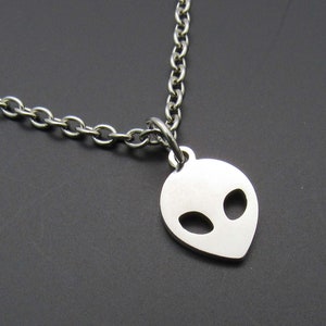 May include: A silver chain necklace with a silver alien head pendant. The pendant is a simple outline of an alien head with two large eyes.