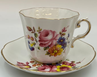 Puede incluir: Una taza de té y un platillo blancos con un patrón floral. La taza tiene un borde dorado y un asa. El platillo tiene un borde dorado y un patrón floral.