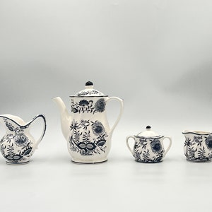 May include: A white teapot, creamer, and sugar bowl with a blue and white floral pattern. The set is made of ceramic and has a classic design.