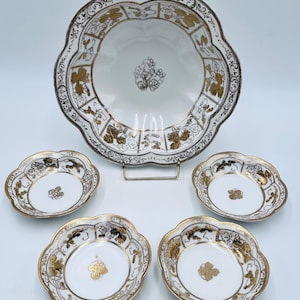 May include: A set of five white porcelain bowls with gold and black floral designs. The bowls are in a graduated size, with the largest bowl in the center and four smaller bowls surrounding it.