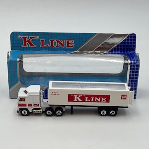 May include: A white toy semi-truck with a trailer featuring the red K LINE logo and text commemorating the first K Line Westbound Double Stack Train into Portland, Oregon, March 19, 1987. The truck is displayed in front of its blue box.