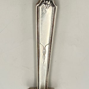 May include: Silver serving fork with an ornate handle and a decorative design. The handle is silver and has a floral design at the top. The fork has a long, thin blade.