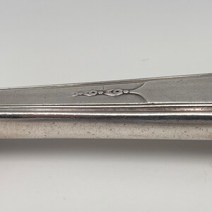 May include: Close-up of the handle of a silver fork with a decorative design.